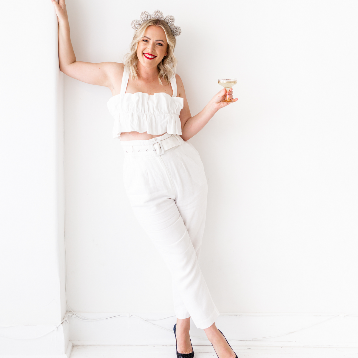Silver Francesca Crown modelled on the head of a female in a white suit. She is holding a champagne glass and leaning casually against a white wall.